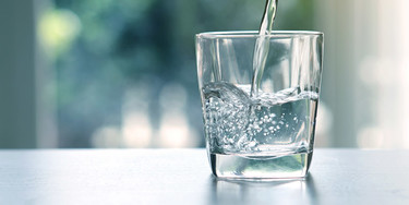 Ein Wasserglas steht auf einem Tisch und wird befüllt
